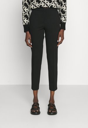 Pantaloni neri su misura con vestibilità slim, vita alta e caviglie a gamba corta. Tessuto liscio con un delicato splendore, abbinati a sandali neri con strap.