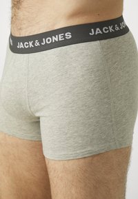 Graue Baumwollboxershorts mit einem schwarzen Bündchen, auf dem "JACK & JONES" in weißer Schrift steht. Der Stoff ist glatt mit einer leichten Textur.
