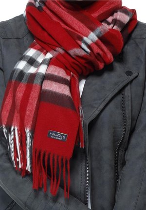 Écharpe à carreaux rouge, noire et blanche avec franges, enroulée autour du cou sur une veste gris foncé avec fermeture éclair et détails de boutons.