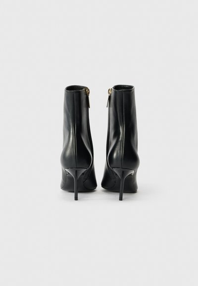 Botas de tobillo de cuero negro con un diseño elegante, punta afilada y tacón de aguja. Presenta un cierre lateral y una textura suave.