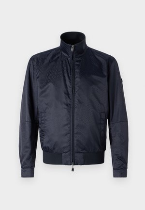 Casaco azul-marinho com fecho de correr à frente, colarinho alto, superfície texturizada, punhos elásticos e cintura elástica; inclui bolsos laterais e detalhe de marca discreto.