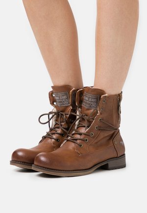 Bottines en cuir marron avec un laçage à l'avant et une fermeture éclair sur le côté. Comprend une pointe ronde, une surface texturée et une étiquette de langue de marque.