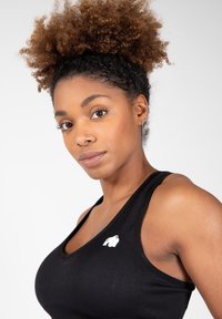 Černý sportovní tílko s závodním výstřihem, vyrobené z hladké tkaniny, s malým bílým logem na levém prsou.