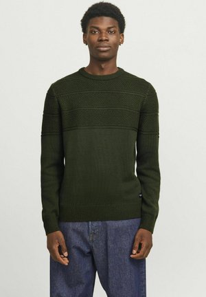 Donkergroen gebreid sweater met textuurpatronen, ronde halslijn en geribde zoom en manchetten. Gepaard met blauwe spijkerbroeken.