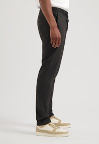 Zwarte elastische broek met een slanke pasvorm, met zijzakken en een soepele, gestructureerde stof. Draag ik met lichtbruine sneakers.