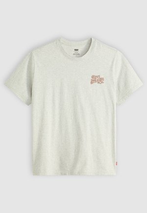 Tricou din bumbac de un gri deschis, cu un mic logo roșu-maro "Levi Strauss & Co." pe partea stângă a pieptului, guler clasic și mâneci scurte.