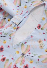 Ljusblått tyg med blommiga och trollsländemönster, med en mjuk textur och en V-ringning som är säkrad med en liten tygslinga.