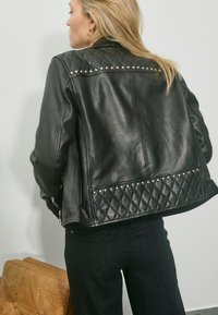 Veste en cuir noire avec un design matelassé et des accents cloutés sur les épaules, vue de dos.