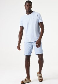 Camiseta de algodón azul claro y pantalones cortos a juego, ambos con dobladillos enrollados. Combinados con sandalias beige que tienen dos tiras ajustables.