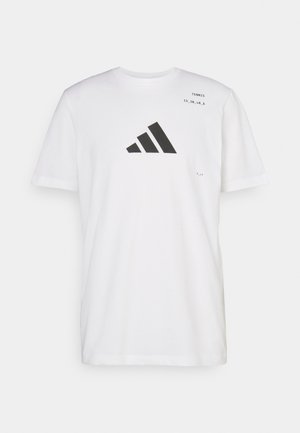Balta medvilninė marškinėliai su dideliu juodu Adidas logotipu, apvalia iškirpte, trumpomis rankovėmis ir spaudiniu šalia peties.