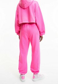 Rosa kapad hoodie och matchande joggers gjorda av mjukt material. Har elastiska ärmslut och midjeband, tillsammans med sportiga vita sneakers.