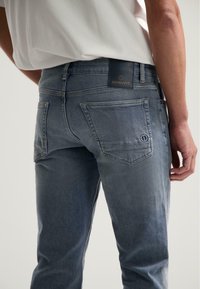Pantalones vaqueros de mezclilla en azul desvaído con un ligero aspecto desgastado. Cuenta con dos bolsillos traseros y una etiqueta de cuero de la marca en la cintura.