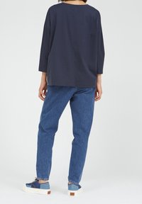 Navy puuvillane pikkade varrukatega topp, mis on koos siniste denimiste teksade ja siniste spordijalatsitega, näidates lõdva istuvuse ja lihtsat disaini.