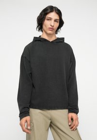 Sort hættetrøje med lange ærmer, afslappet pasform og blød tekstur. Har et simpelt design og fremtrædende syninger.