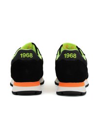 Scarpe da ginnastica nere con accenti verdi, con tomaia testurizzata, collo imbottito e suola intermedia arancione. Numero "1968" visibile sui talloni.