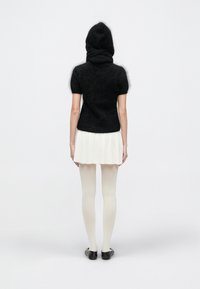 Bluză neagră tricotată cu glugă, mâneci scurte și corp mulat. Asortată cu o fustă albă evazată și colanți deschiși la culoare, purtată cu pantofi negri.