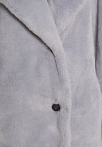 Mjuk grå fuskpälsjacka med slagkrage, som har en enkel svart knappstängning och en texturerad, plyschyta.