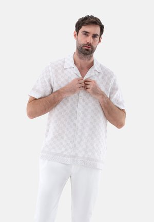 Camicia bianca a maniche corte con un motivo a texture sottile e colletto, abbinata a pantaloni bianchi.