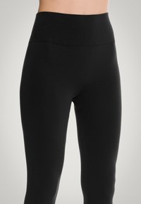 Leggings neri a vita alta realizzati in materiale elasticizzato. Presentano una texture liscia e un design senza cuciture, che si restringe verso le caviglie.