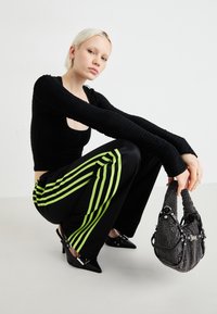 Melnas ribotās garas piedurknes augšdaļa, šaura piegriezuma. Melni bikses ar neona zaļām svītrām. Norādīti melni papēži. Melna studēta rokassoma ar īsu rokturi.