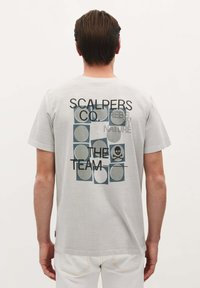 Grijze katoenen t-shirt met een grafisch ontwerp op de achterkant met de tekst "SCALPERS CO. REBEL BY NATURE" en een schedelicoon tussen cirkelvormige patronen.