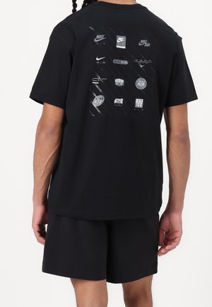 Personne portant un t-shirt noir avec plusieurs logos Nike Air disposés en grille dans le dos, associé à un short noir.