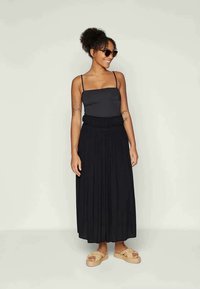 Black pleated maxi skirt with elasticated waist paired with a fitted black tank top. Worn with tan slip-on platform sandals.