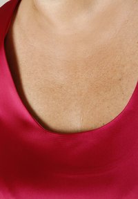 Close-up of a neckline with smooth skin wearing a deep red satin garment.