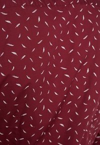 Tessuto bordeaux con un sottile motivo di piccole piume bianche e forme simili a grano, texture liscia e finitura tessuta.