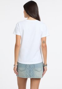 Camiseta blanca de manga corta con cuello redondo, llevada con una falda de mezclilla azul claro que presenta un dobladillo deshilachado y bolsillos traseros.