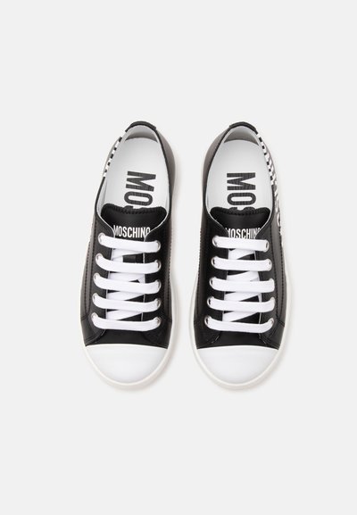 Paire de baskets basses noir et blanc avec des lacets blancs et le logo "MOSCHINO" sur les languettes et les semelles intérieures, vue de dessus.