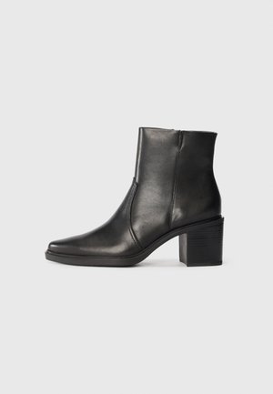 Sorte lær ankle boot med spiss tå og en mellomhøy blokkhelt. Har en glatt tekstur og en detalj med sidesøm.