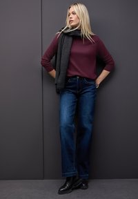 Bordeaux langærmet top parret med mørkeblå vide jeans. Accessoriseret med et mørkegråt tørklæde og sorte ankelstøvler. Glatte teksturer.