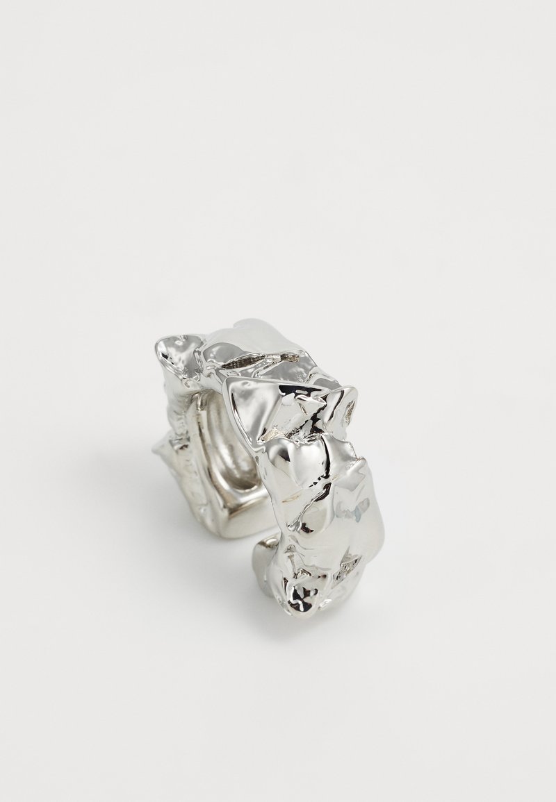 Bague en argent massif avec un design texturé et irrégulier. Fabriquée en métal brillant, elle présente une sensation sculpturale en relief avec des bords distincts.