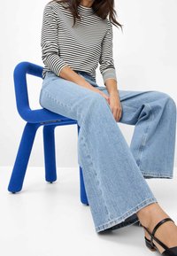 Light blue wide-leg jeans made of denim, paired with a black and white striped turtleneck. Seated on a blue, foam chair.