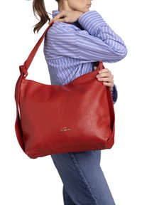 Rode leren schoudertas met een gestructureerde afwerking, voorzien van een lange schouderriem en een gouden logo aan de voorkant. Compact en praktisch ontwerp.