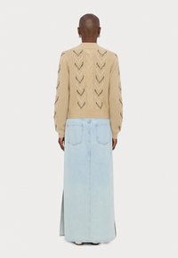 Piscinebeige kootud kampsun avatud töötlusega ja pikkade varrukatega, millele on sobitatud helesinine denim pikklehemüts tagakotitega ja külje lõhega.