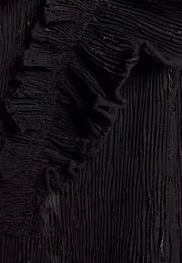 Tissu noir transparent avec plis verticaux et bord volanté montrant des détails texturés et translucides.