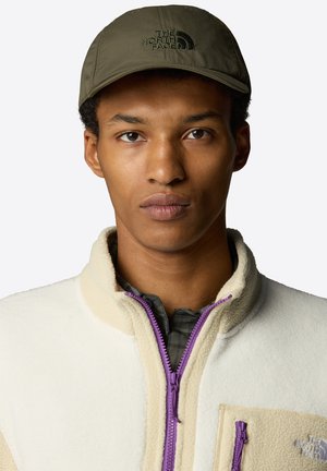 Olive green cap with embroidered logo, worn with a beige fleece jacket featuring purple zip and detailing, over a plaid shirt.