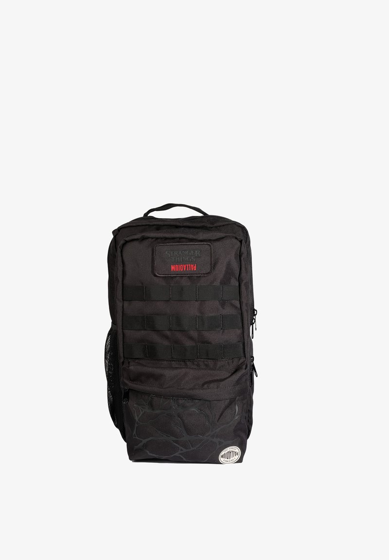Sac à dos rectangulaire noir avec plusieurs compartiments zippés, bretelles en sangle, poche latérale en filet et patchs de marque indiquant "Stranger Things" et "Palladium".