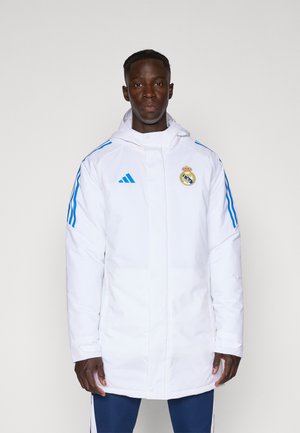 Hvid isoleret jakke med hætte, med blå striber og Real Madrid-logo. Lavet af glat stof, med lige snit og lynlås lukning.