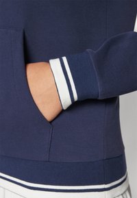 Marinblå sweatshirt med texturerad tyg, med en framficka och randiga vita och blå manchetter.