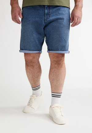 Donkere blauwe denim shorts met opgerolde boorden, gecombineerd met witte sneakers en gestreepte sportsokken. De stof heeft een gladde textuur.