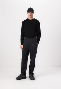 Black sweater, dark grey sweatpants with elastic waistband and embroidered detail, and black sneakers on a model against a white background.