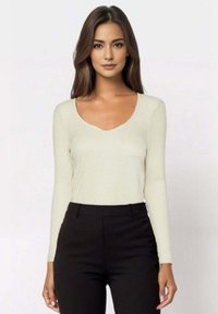 Top a maniche lunghe, color beige chiaro, con scollatura a V profonda e texture a coste, abbinato a pantaloni neri a vita alta.