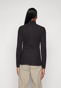 Black long-sleeve top with a textured fabric, high collar, and side slits. The design features a clean, fitted silhouette.