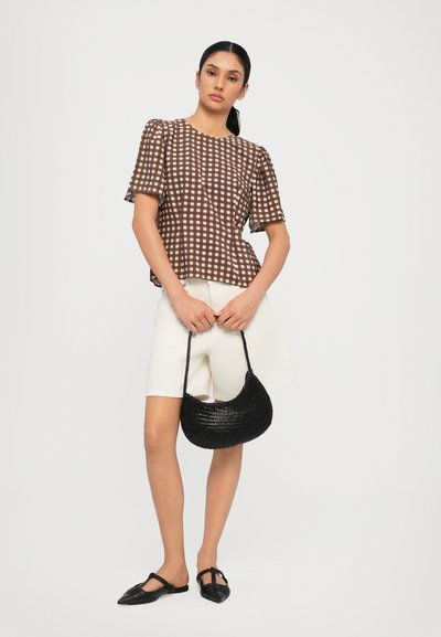 Top de manga corta a cuadros marrones, pantalones cortos crema, bolso de tela negro y zapatos planos negros con punta, sobre un fondo claro.