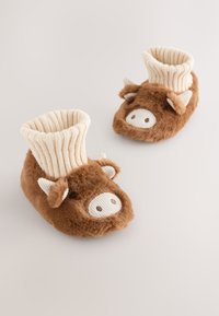 Chaussons en peluche marron avec des poignets côtelés crème, présentant un motif de visage de vache, des oreilles et des narines. Texture douce et forme ronde.