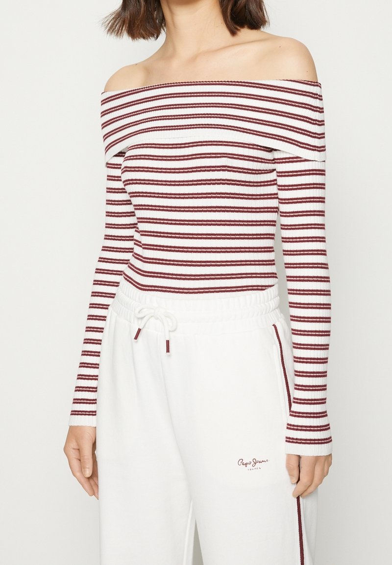 Top scollato con strisce orizzontali bordeaux e bianche, texture a costine, abbinato a pantaloni jogger bianchi con dettaglio rosso.