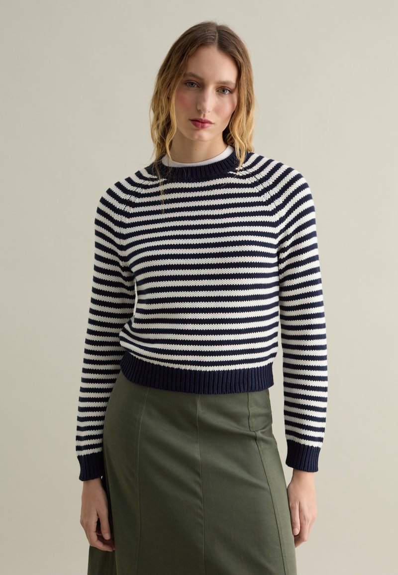 Maglione lavorato a maglia con righe blu navy e bianche, polsini e orlo a costine, scollatura rotonda, abbinato a una gonna verde.